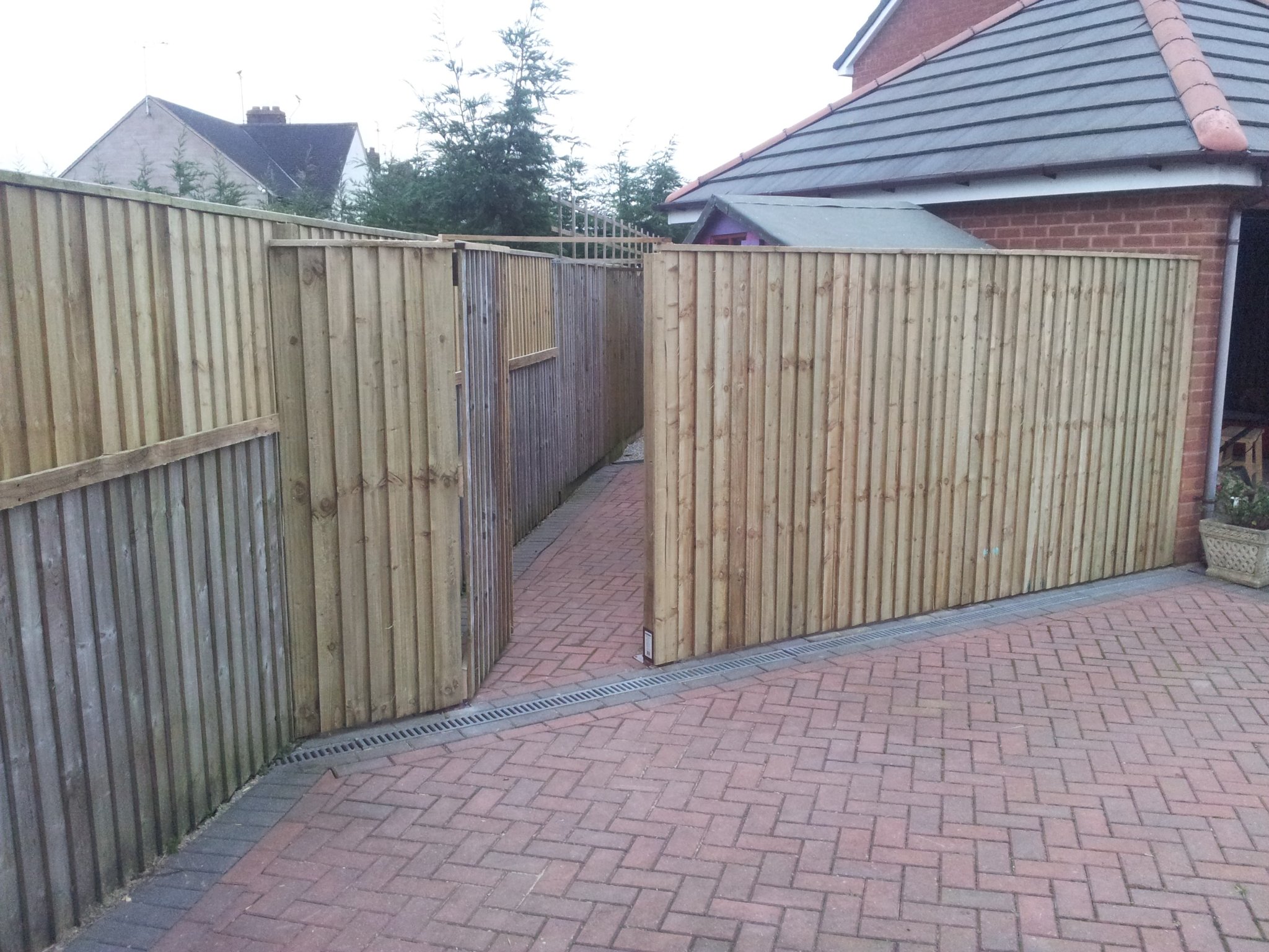 Tall close-board fencing and gate along a block-paved drive